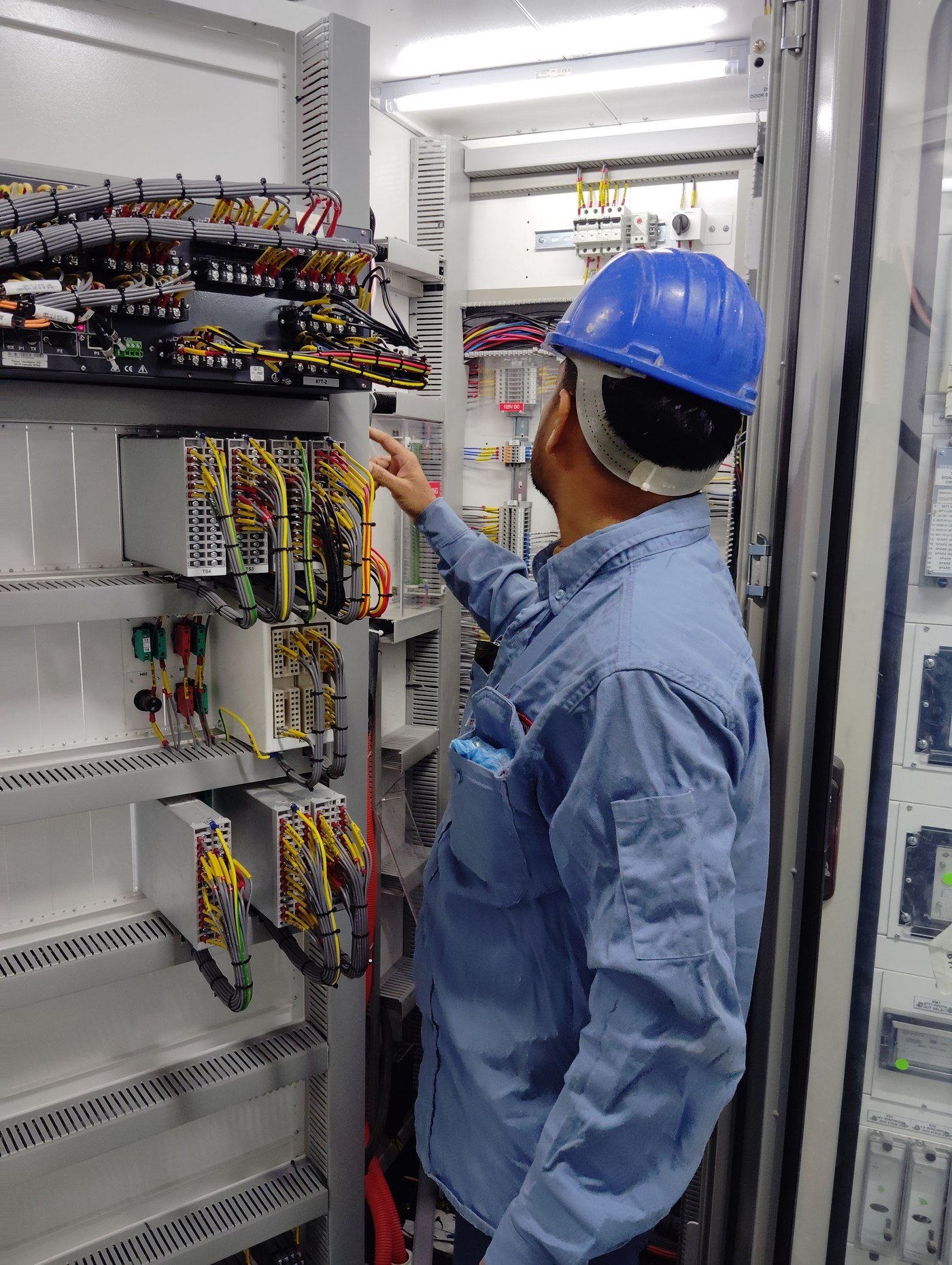 Symbolfoto: Elektrofachkraft mit Schutzhelm kontrolliert einen Schaltschrank